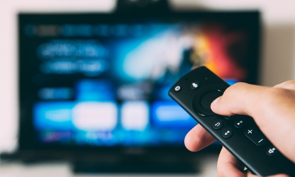 A remote control pointed at the tv with a streaming service on it. Photo courtesy of Glen Carstens-Peters on Unsplash.