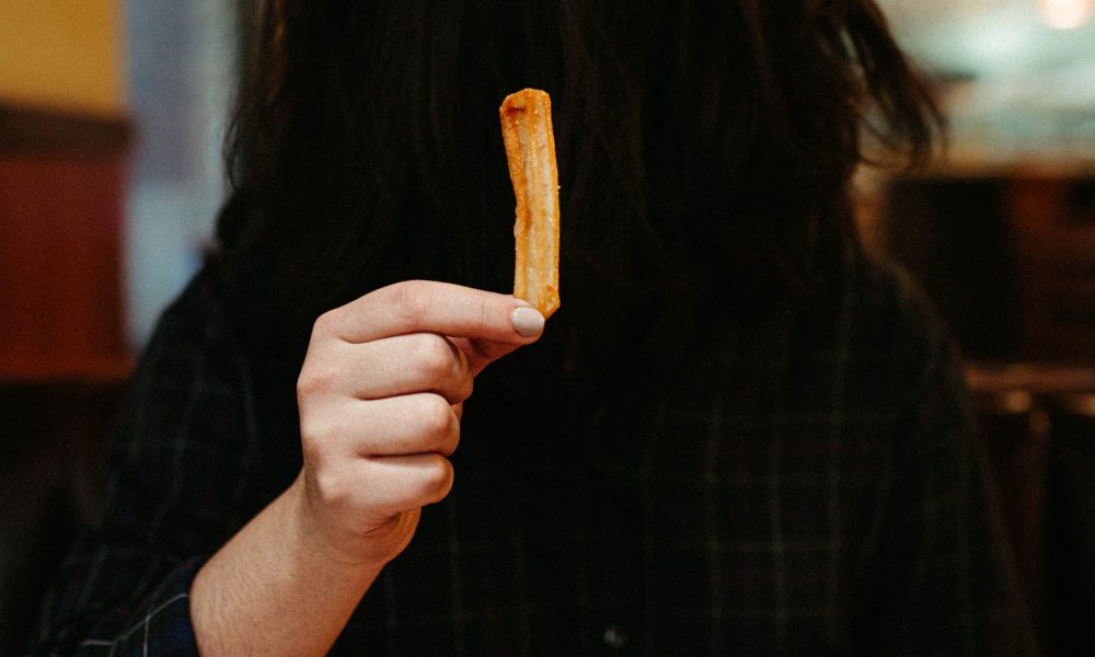 Someone holding up a french fry with their face covered by their hair. Photo courtesy of Jesus Rocha on Unsplash.
