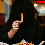 Someone holding up a french fry with their face covered by their hair. Photo courtesy of Jesus Rocha on Unsplash.