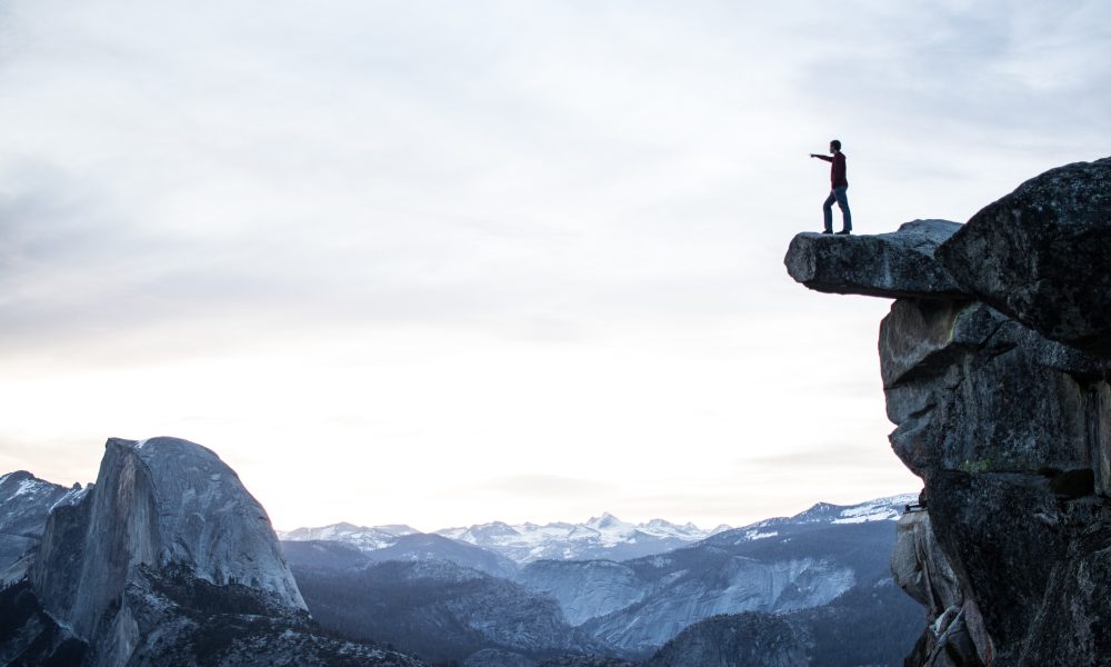 Man standing on a cliff pointing. Photo courtesy of Jeremy Perkins on Unsplash.