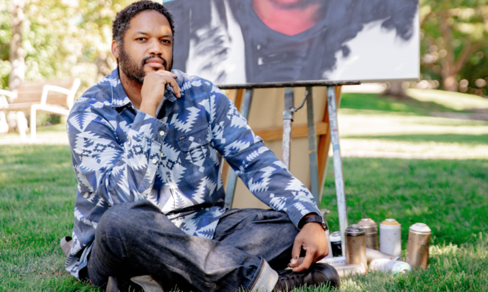 Image of Jason Talbot sitting on grass with painting behind him