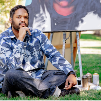 Image of Jason Talbot sitting on grass with painting behind him