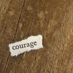 Ripped paper that has the word courage on it. Photo courtesy of Michael Dziedzic on Unsplash.