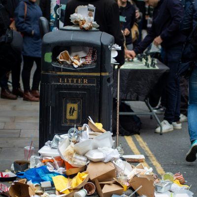 Photo of food waste on the ground next to a trash bin on a sidewalk. Photo courtesy of Paul Schellekens on Unsplash.