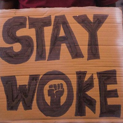 Man Wearing a Hat Holding a Placard with a Text Stay Woke. Photo courtesy of FPD Images on Pexels.