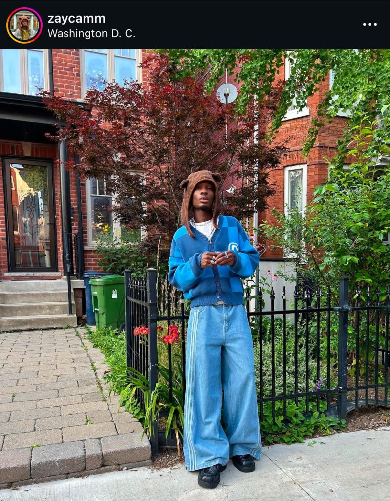 Fashion Instagram post of a Black teen wearing a furry brown hat with bear ears, a blue checked sweater, baggie blue jeans with stripes on the sides, and brown nondescript shoes. 