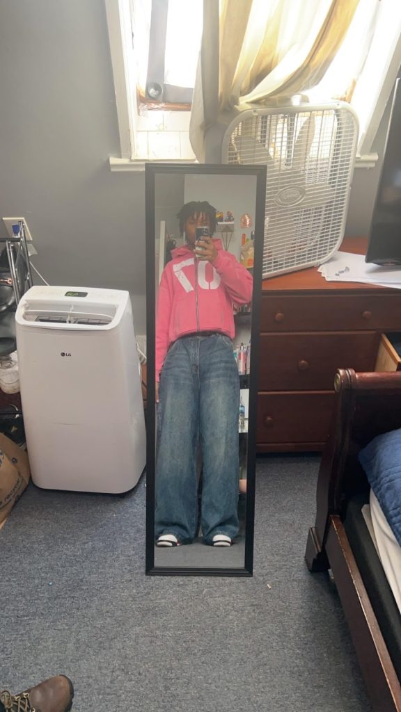Full length mirror selfie of the author, a Black teen, wearing baggie pants and a cropped pink 70 hoodie.