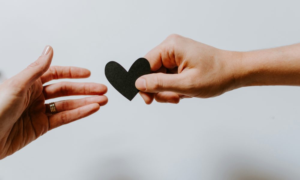 Photo of one hand handing another hand a black heart courtesy of Kelly Sikkema on Unsplash.