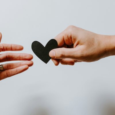 Photo of one hand handing another hand a black heart courtesy of Kelly Sikkema on Unsplash.