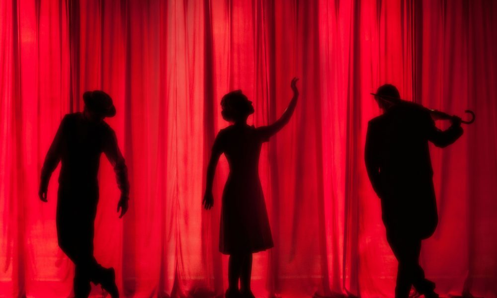 Photo of three actors behind a stage curtain courtesy of Kyle Head on Unsplash.