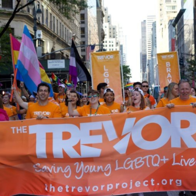 People at a protest in a metropolitan area, carrying an orange banner with the Trevor Project's name and logo.