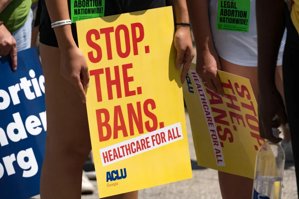 Sign held at a protest that reads "stop. the. bans. healthcare for all."