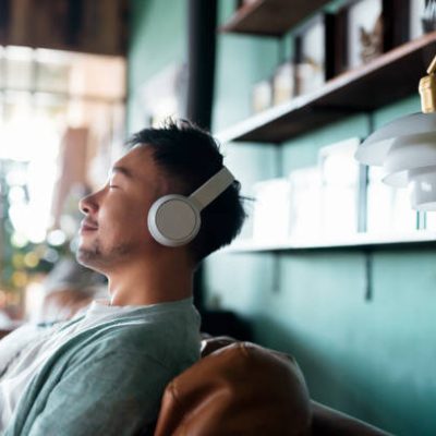 Young Asian man with eyes closed, enjoying music over headphones while relaxing on the sofa at home