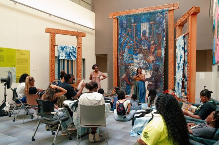 Students seated for a presentation on woven artworks.