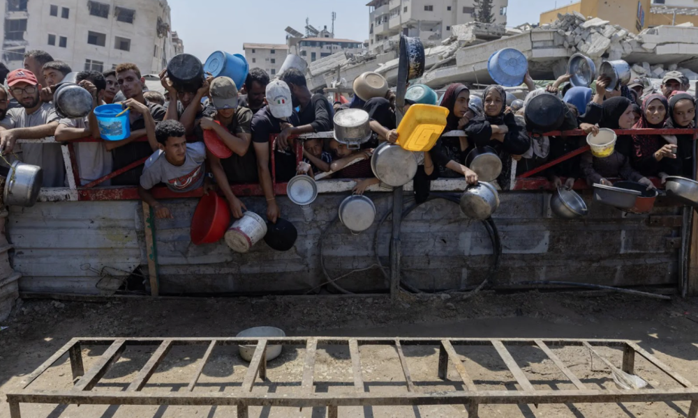 Hungry people carrying plastic containers crowd around a food distribution site in Gaza.