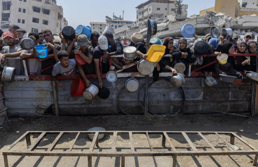 Hungry people carrying plastic containers crowd around a food distribution site in Gaza.