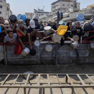 Hungry people carrying plastic containers crowd around a food distribution site in Gaza.