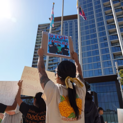 Photograph of an protest against deportation in an urban area. Focused on a woman holding up a sign that reads 'stop seperating immigrant families.'