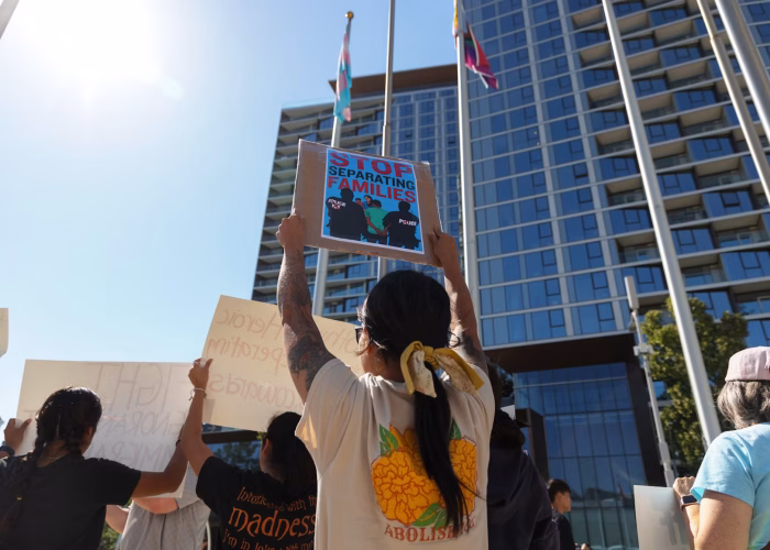Photograph of an protest against deportation in an urban area. Focused on a woman holding up a sign that reads 'stop seperating immigrant families.'