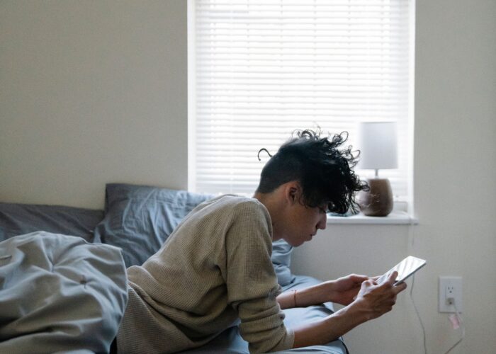 Teen boy sitting on his bed looking at his smartphone.
