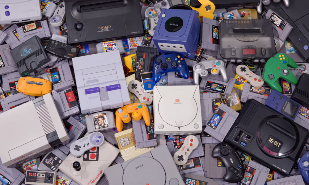 Photo of several retro gaming consoles and game cartridges in a scattered pile