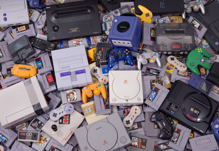 Photo of several retro gaming consoles and game cartridges in a scattered pile